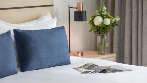 a bed with a blue pillow and a vase of flowers at Oaks Adelaide Embassy Suites in Adelaide