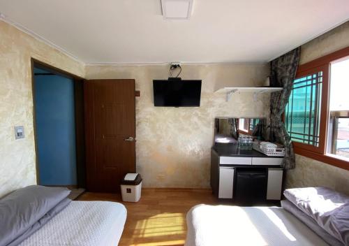 a bedroom with two beds and a desk and a television at Gudeok Guesthouse in Seogwipo