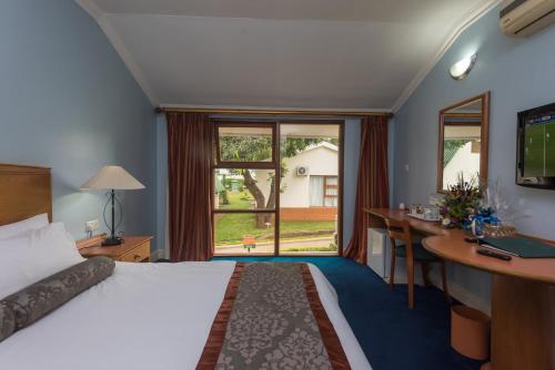 a hotel room with a bed and a desk and a window at Sunbird Lilongwe in Lilongwe