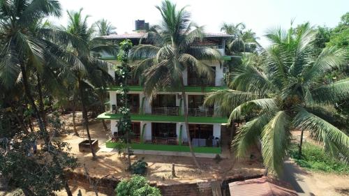 a green house with palm trees in front of it at John's Highland Comfort (Guest House) in Majorda