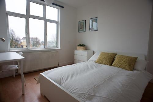 ein weißes Schlafzimmer mit einem Bett und zwei Fenstern in der Unterkunft Tooting Bec Rooms by DC London Rooms in London