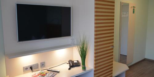 a television on a wall above a desk with a phone at Hotel Bergwirt in Herrieden