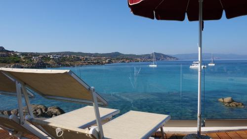 a beach chair with an umbrella and the ocean at Club Esse Shardana in Santa Teresa Gallura