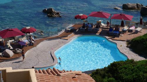 a swimming pool with umbrellas and the ocean at Club Esse Shardana in Santa Teresa Gallura