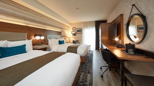 a hotel room with two beds and a desk and a mirror at Stay Inn Hotel Toronto in Toronto