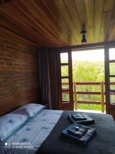 Bett in einem Zimmer mit einem großen Fenster in der Unterkunft Pousada Cachoeira Esmeralda in Luminárias