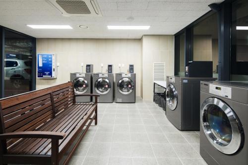a row of washing machines and a bench in a laundry room at Orakai Cheonggyesan Hotel, BW Premier Collection in Seoul
