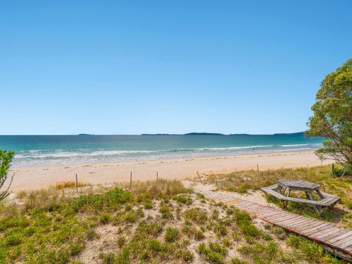 a picnic table on the beach with the ocean in the background at Poppy's Beach House - Beachfront Whangapoua Home in Whangapoua