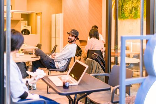 a man sitting at a table with a laptop at &AND HOSTEL ASAKUSA KAPPABASHI in Tokyo