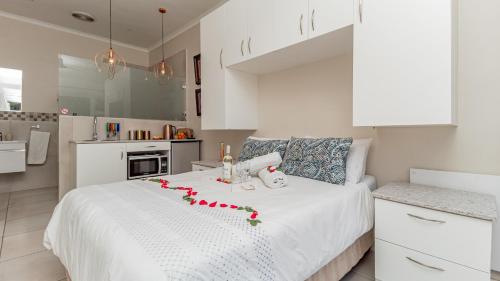 a white bedroom with a white bed with red flowers on it at Sea Breeze Guest House in Bloubergstrand