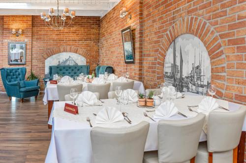 a restaurant with white tables and chairs and a brick wall at Hotel Rigga in Władysławowo
