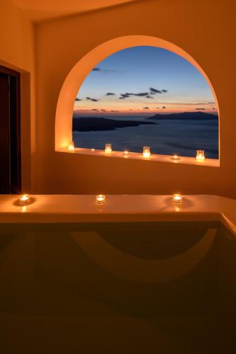 a bathroom with a window and a tub with candles at Panorama Suites in Fira