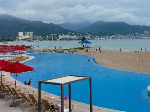 a large swimming pool next to a beach with chairs and umbrellas at Apartamentos Grand Venetian Puerto Vallarta in Puerto Vallarta