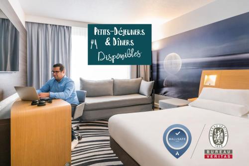 a man sitting in a hotel room with a laptop at Novotel Saclay in Saclay