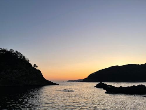 a sunset over a body of water with rocks at Guesthouse All you need - All rooms have an ocean view! in Shimoda