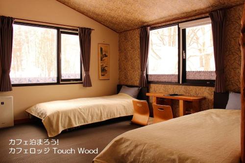 美瑛的住宿－カフェロッジ Touch Wood，客房设有两张床、一张桌子和两个窗户。