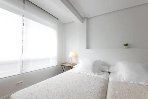 a white bedroom with two beds and a window at ONDARRETA ROOM with independent entrance in San Sebastián