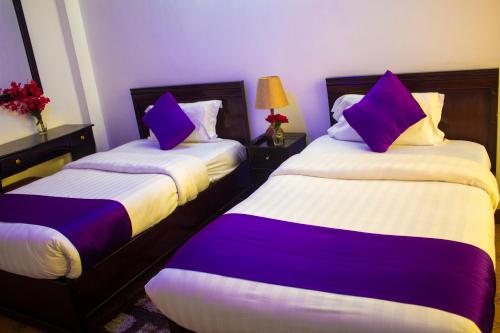 two beds in a hotel room with purple pillows at New Hotel Aquiline in Arusha