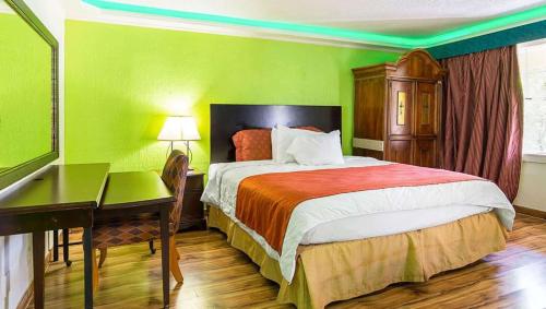 1 dormitorio con 1 cama con escritorio y pared verde en Magnuson Hotel Little Rock South en Little Rock