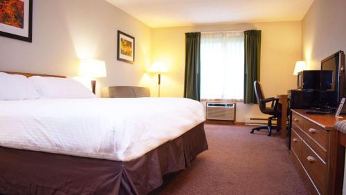 a hotel room with a bed and a desk and a television at Magnuson Hotel Country Inn in Ishpeming