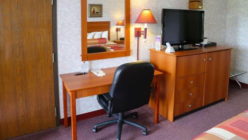 a room with a desk with a television and a bedroom at Magnuson Hotel Howell/Brighton in Howell