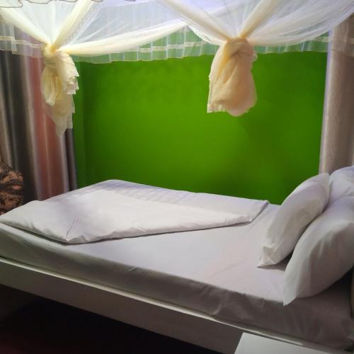 a bed with white sheets and a green wall at Bethel Resort & Hotels in Gulu