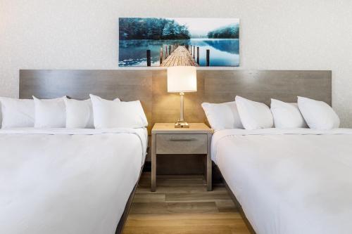 two beds in a hotel room next to a table with a lamp at Repotel Henri IV Québec in Quebec City