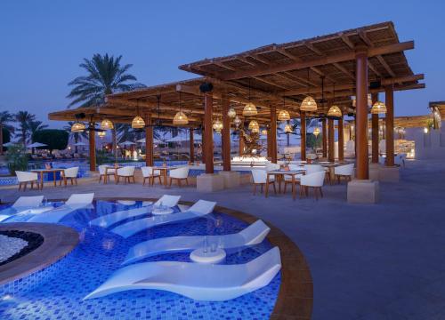 un complejo con piscina, mesas y sillas en Anantara Qasr al Sarab Desert Resort, en Jurayrah