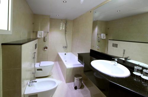 een badkamer met 2 wastafels, een toilet en een bad bij Gulf Inn Hotel Deira Formerly City Star Hotel in Dubai