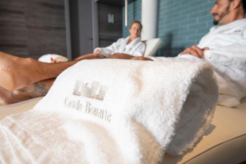 a man laying on a bed with a white blanket at Castello Bonaria Wine & Spa Resort in Campiglia Marittima