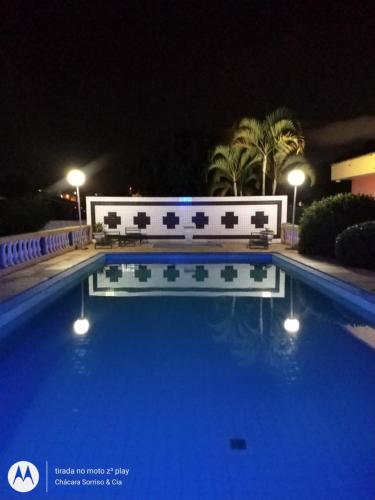 a blue swimming pool at night with lights and palm trees at Chácara Sorriso 1 em Atibaia in Atibaia