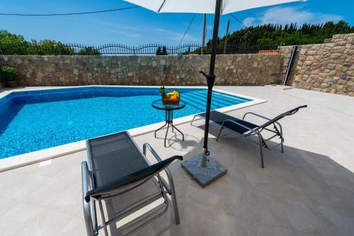 eine Terrasse mit 2 Stühlen und einem Sonnenschirm neben einem Pool in der Unterkunft Apartments Villa Kabalero in Gruda
