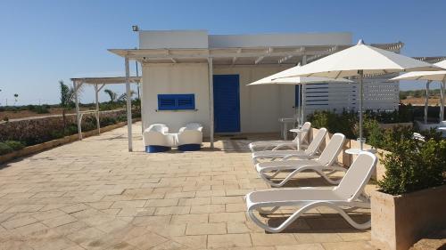 a row of white lounge chairs and an umbrella at Ville Torre del Pizzo in Gallipoli