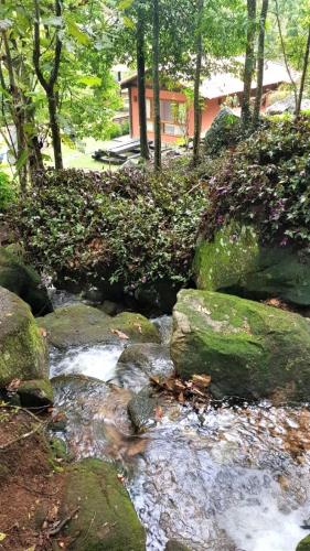 a stream of water with rocks in front of a house at Tékinfin, você chegou! Lindo sítio em Secretário! in Petrópolis