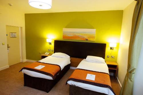 two beds in a hotel room with yellow walls at The Twelve Knights in Port Talbot