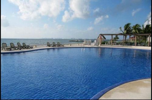 a large swimming pool with chairs and the ocean at Relaxing beachfront loft in Cancún