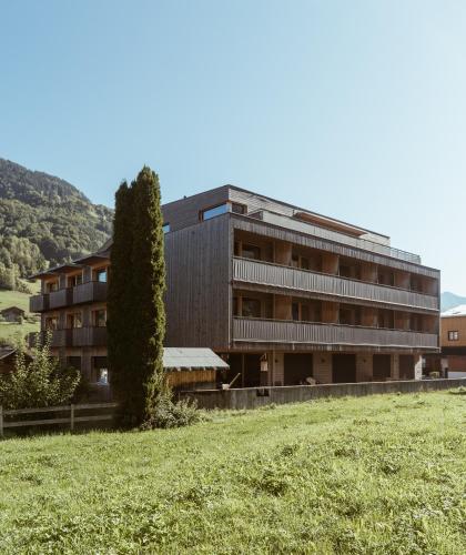 a building with a tree in front of a field at Aparthotel Hubertus Mellau in Mellau