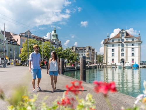 a man and woman walking on a sidewalk next to a river at Hotel de Charme Römerhof in Arbon