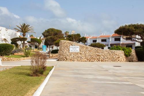a stone wall with a sign next to a sidewalk at El Faro 8 in Cala'n Bosch