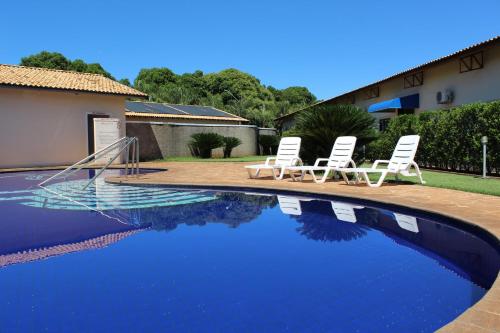 two white chairs and a swimming pool with a house at Grandes Lagos Park Hotel in Jales