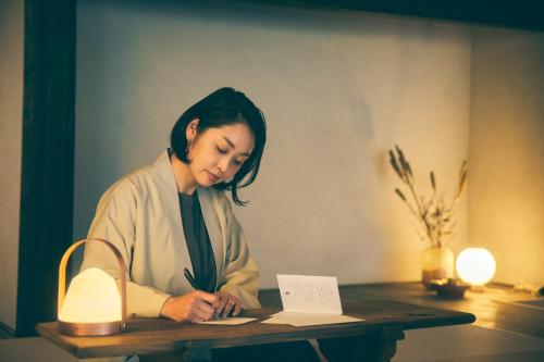 a woman sitting at a desk writing on a paper at Kominkayado LOOF Kyonoie in Ōwatari