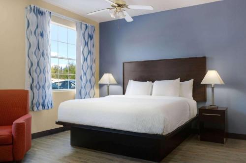 a bedroom with a bed and a chair and a window at Days Inn & Suites by Wyndham DFW Airport South-Euless in Euless