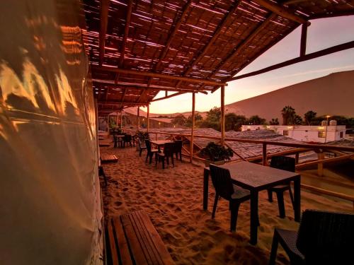 a patio with tables and chairs with the sunset in the background at Ecocamp Huacachina in Ica