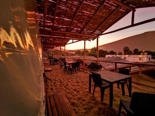 un patio con mesas y sillas con la puesta de sol en el fondo en Ecocamp Huacachina, en Ica