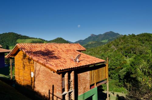 a building with a red roof with mountains in the background at Pousada Lua de Minas in Visconde De Maua