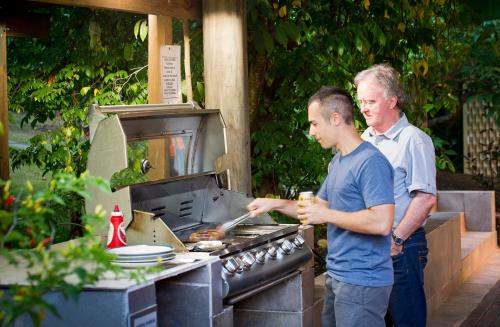 dwóch mężczyzn przygotowujących jedzenie na grillu w ogrodzie w obiekcie Glass House Mountains Ecolodge w mieście Glass House Mountains