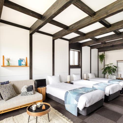 two beds and a couch in a room with wooden ceilings at JINYA Fujikawaguchiko in Fujikawaguchiko