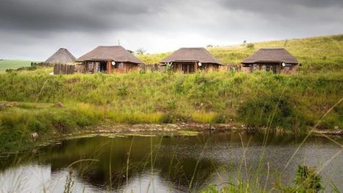 a group of huts on a hill next to a body of water at Rain Farm Game Lodge in uMhlali