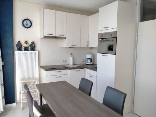 a kitchen with white cabinets and a wooden table with chairs at Studio Penthouse Nieuwpoort in Nieuwpoort