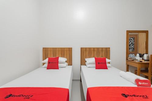 two beds with red pillows in a room at RedDoorz Syariah Plus @ Perintis Guesthouse Tasikmalaya in Tasikmalaya